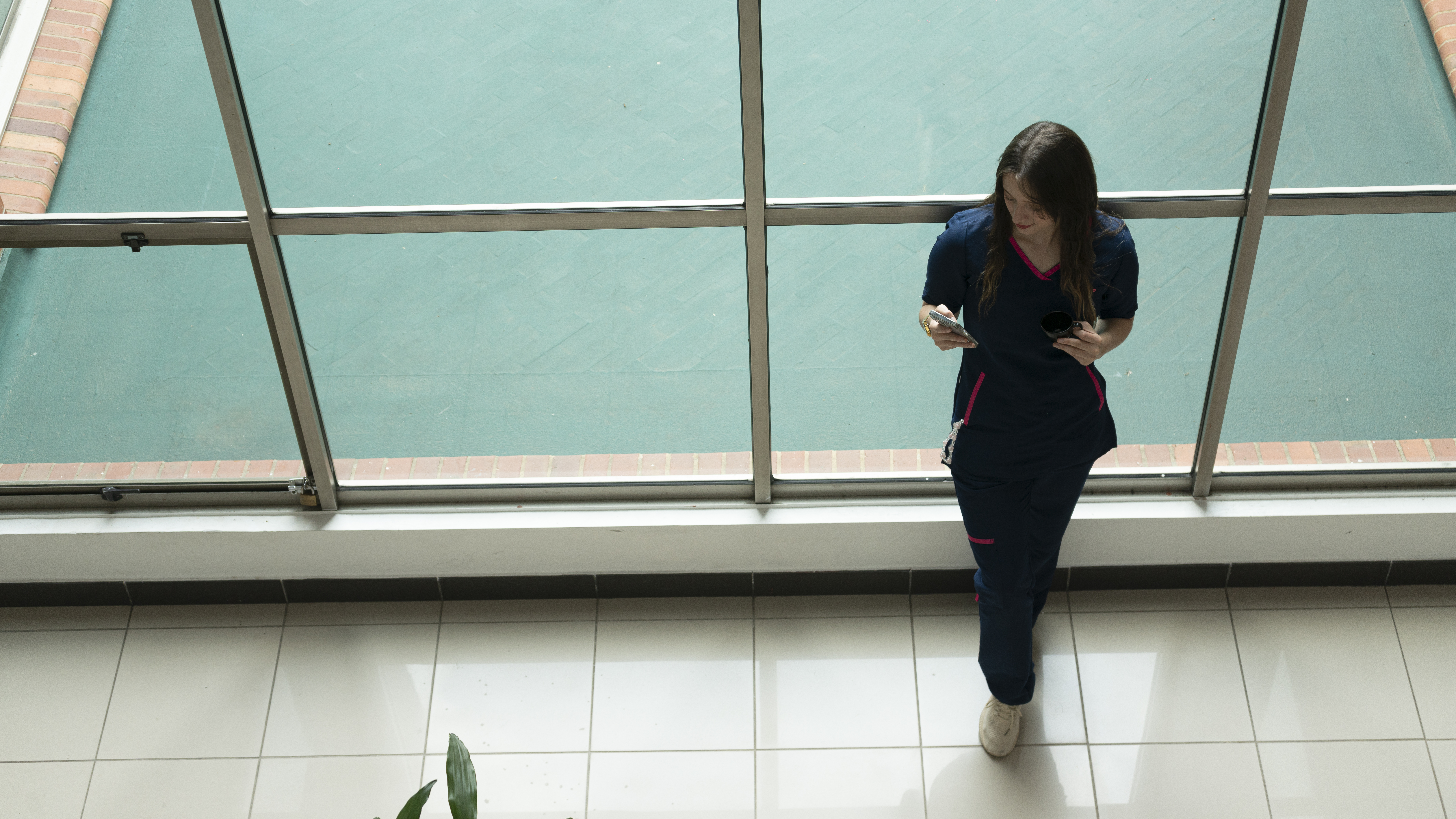 Nurse standing in a hallway alone holding a phone.